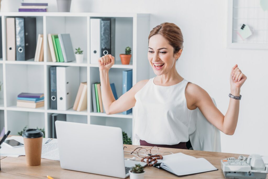 successful businesswoman celebrating at workplace and looking at laptop